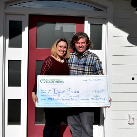 Couple holding big check in front of home