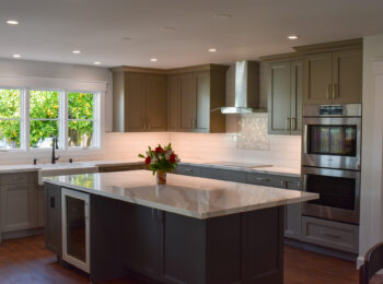image of an inside of a kitchen with a large marble top island, pretty cabinets and a lemon tree outside the window